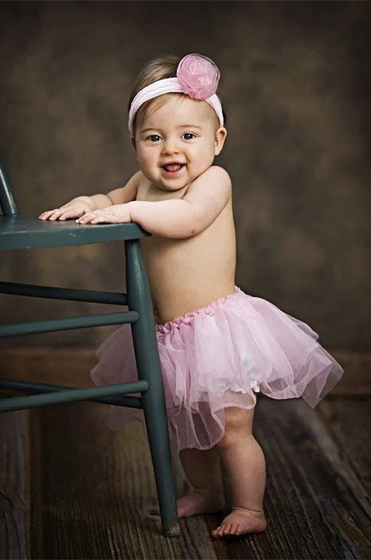 Small girl in pink skirt standing beside a chair